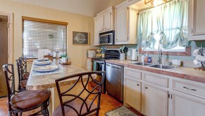 A kitchen with white cabinets, a stove, microwave, and a dishwasher. There is a dining table with chairs and a window with blinds. - 1/2 Mi to Lake Lawtonka: Mtn-view Haven! (Medicine Park)