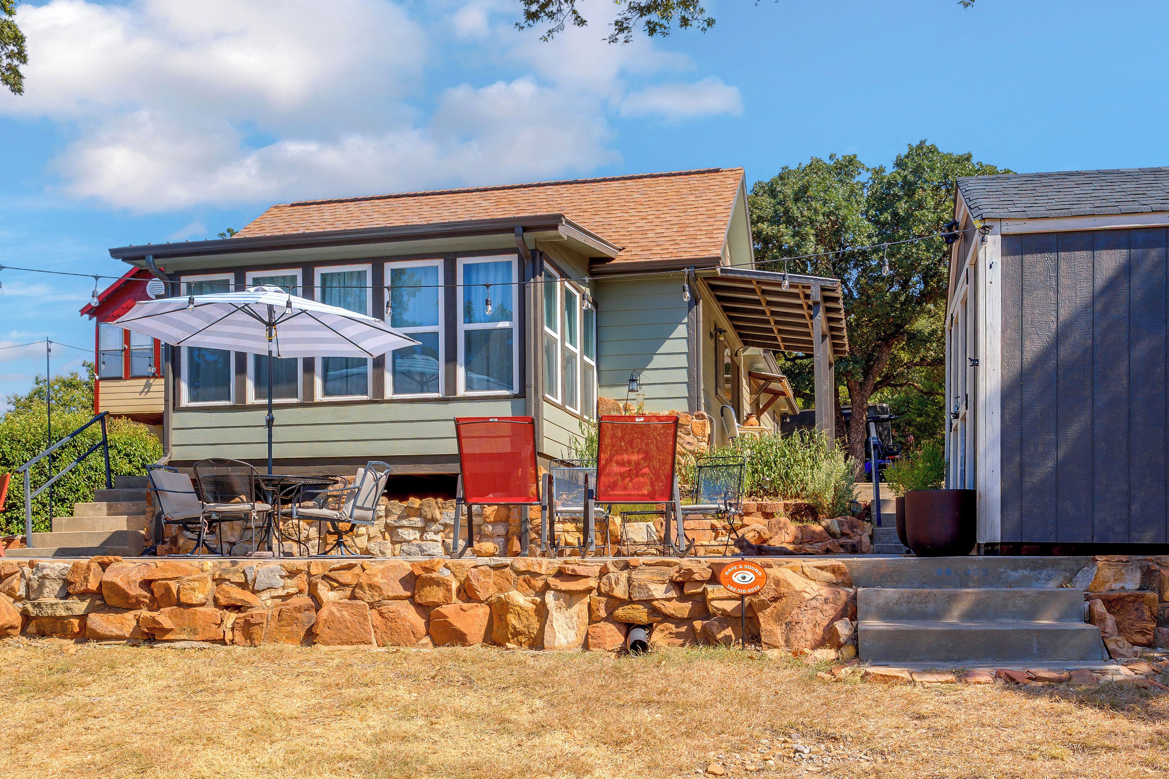 A house with a stone wall, a covered patio with chairs, and a small shed.