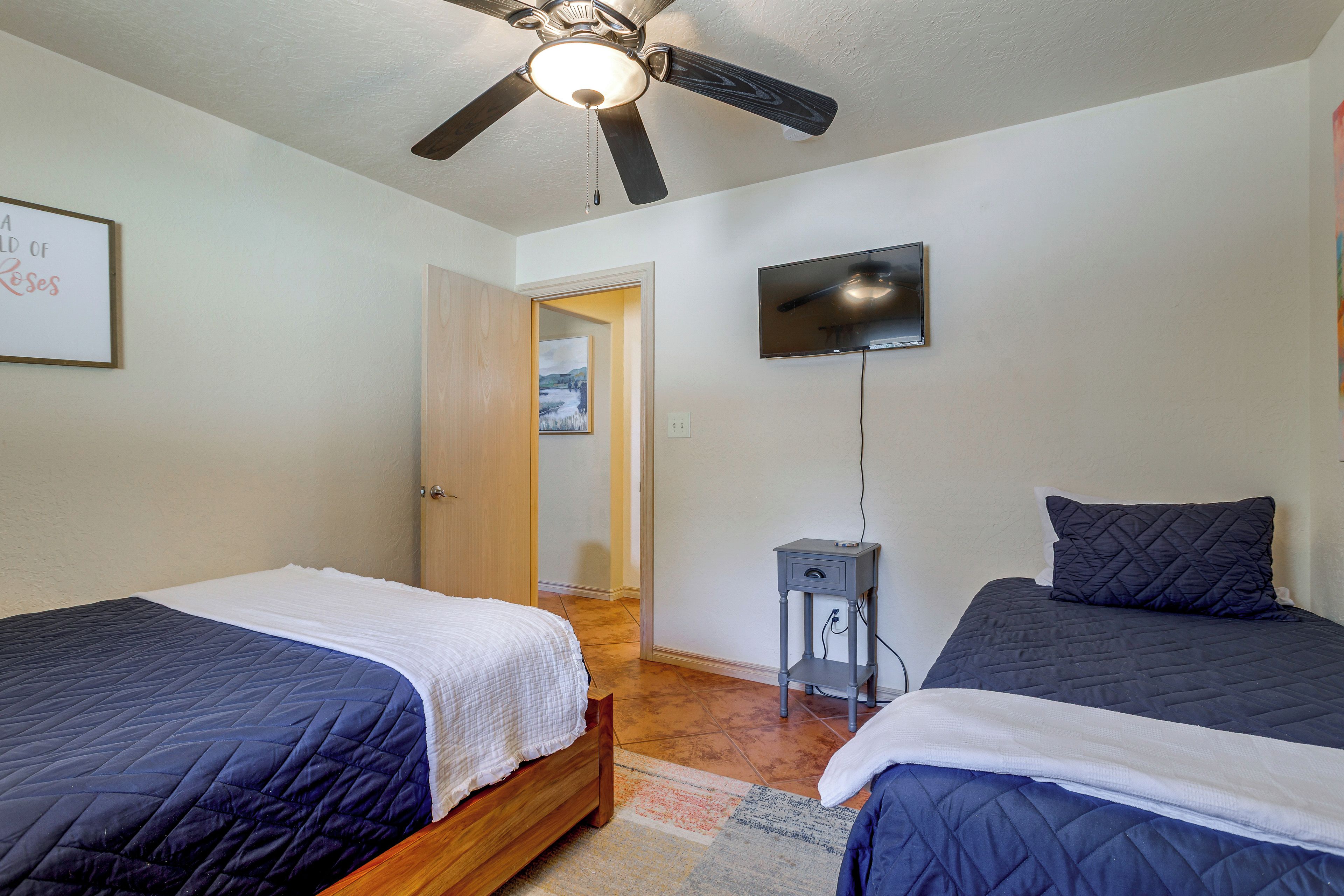 A bedroom with two beds, a ceiling fan, a TV, and a door leading to another room.