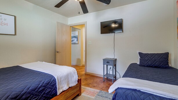 A bedroom with two beds, a ceiling fan, a TV, and a door leading to another room. - 1/2 Mi to Lake Lawtonka: Mtn-view Haven! (Medicine Park)