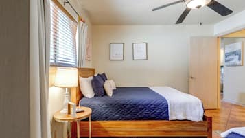 A bedroom with a bed, a bedside table with a lamp, a ceiling fan, and two framed pictures on the wall.