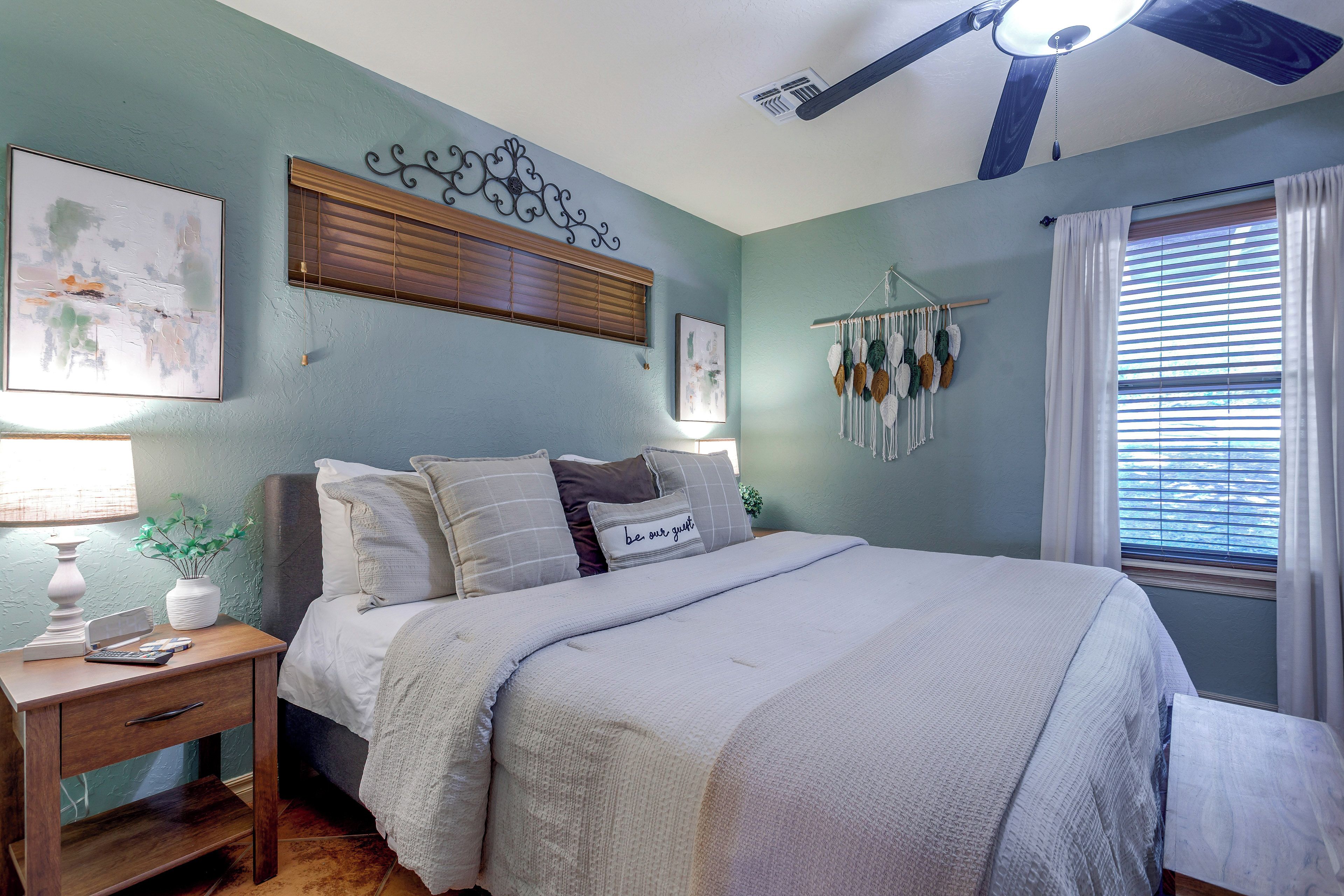 Un dormitorio con cama, mesita de noche, lámpara, decoración en la pared y ventilador de techo.