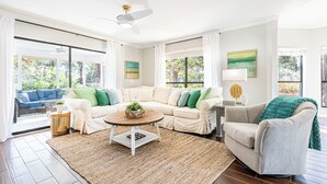 Un salón espacioso con un sofá seccional color beige, una mesa de centro redonda y un gran ventanal con vistas al exterior.