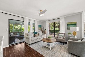 A modern living room with a sofa, armchairs, a coffee table, and a ceiling fan.