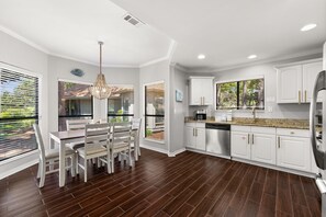 A modern kitchen with white cabinetry, a stainless steel refrigerator, and a dining area with a wooden table and chairs.