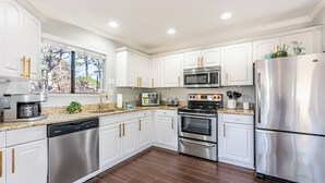 A modern kitchen with white cabinets, stainless steel appliances, and a granite countertop. - Golf Cart ~ Pet Friendly ~ Resort Beach Access (Miramar Beach)