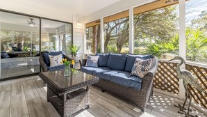 Un patio soleado con un sofá de mimbre, una mesa de vidrio y una escultura decorativa de un pájaro.