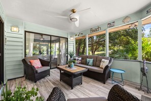 A covered outdoor seating area with wicker furniture, a ceiling fan, and a view of the outdoors.