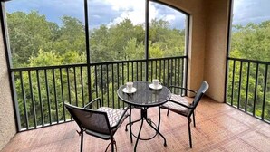 A balcony with a round table and two chairs, offering a view of a forested landscape.