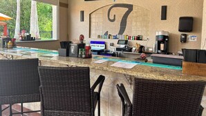 A bar area with a counter, bar stools, a coffee machine, and a television mounted on the wall displaying a program.
