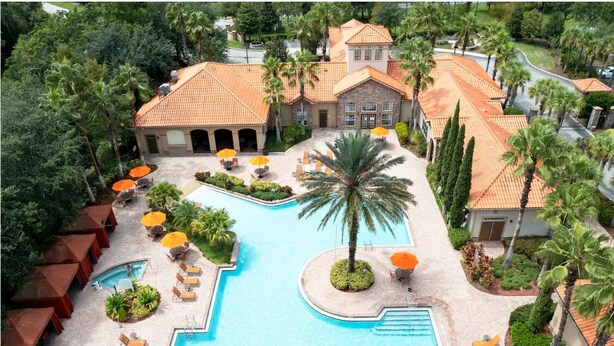 A resort with a swimming pool, sun loungers, palm trees, and a building with a tiled roof.