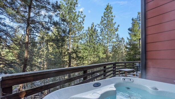 Een hottub op een houten terras met uitzicht op een bos.
