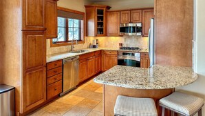 A kitchen with wooden cabinets, a granite countertop, stainless steel appliances, and a window with a view.