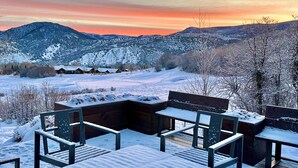 A snowy outdoor seating area with benches and tables, overlooking a snow-covered landscape and distant buildings.
