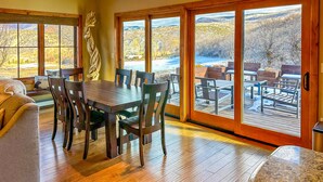 A spacious dining area with a wooden table and chairs, large windows with a view of a snowy landscape, and a cozy seating area with a couch and cushions.