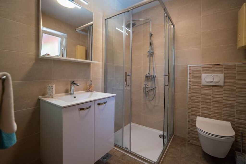 Ein modernes Badezimmer mit einer Glaskabine zur Dusche, einem weißen Waschbecken mit Spiegel darüber und einer Toilette mit wandmontiertem Bidet.