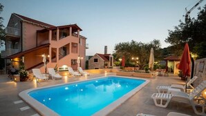 A swimming pool with lounge chairs and umbrellas, surrounded by buildings with balconies and outdoor lighting. - Apartments Njirić - Comfort Studio with Balcony Sea View - No.4 (Zaton)