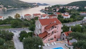 A multi-story hotel with a swimming pool, located near a body of water with a view of the sea and hills. - Apartments Njirić - Comfort Studio with Balcony Sea View - No.4 (Zaton)