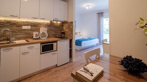 A compact kitchen with white cabinets, a stone backsplash, and a coffee maker. A dining table with a book and glasses is visible. - Apartments Njirić - Comfort Studio with Balcony Sea View - No.4 (Zaton)
