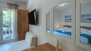 A hotel room with a bed, a wooden desk, a television, and a large mirror reflecting the room. - Apartments Njirić - Comfort Studio with Balcony Sea View - No.4 (Zaton)