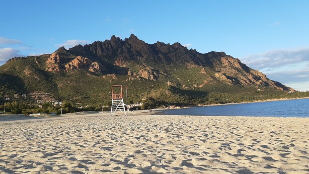 Een strand met een bewakershut, een berg op de achtergrond en een heldere lucht.