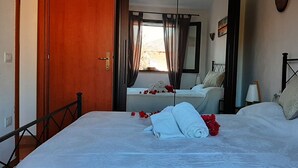 Een slaapkamer met een bed, een houten deur, een raam met gordijnen, een nachtkastje en een bedtafel.