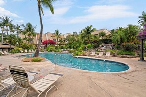 A resort pool area with lounge chairs, palm trees, and a small waterfall feature.
