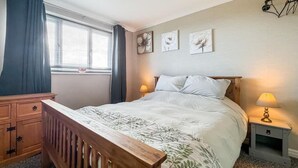 A bedroom with a bed, bedside tables, a dresser, and a window with curtains. - Eco Friendly White House Sleeps 8 (Colwyn Bay)