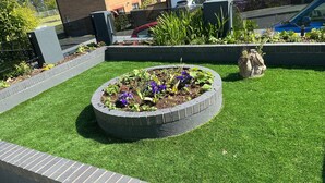 A landscaped garden area with a circular flower bed, surrounded by a brick border. - Eco Friendly White House Sleeps 8 (Colwyn Bay)