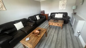 A living room with two black leather sofas, a wooden coffee table, a wooden side table, a white radiator, and a hanging light fixture. - Eco Friendly White House Sleeps 8 (Colwyn Bay)