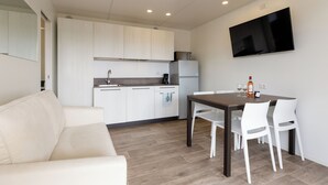 A modern kitchen with white cabinets, a built-in microwave, and a refrigerator. There is a dining table with white chairs and a flat-screen TV mounted on the wall. - Agriturismo Agricamping GARDA NATURA (Costermano sul Garda)