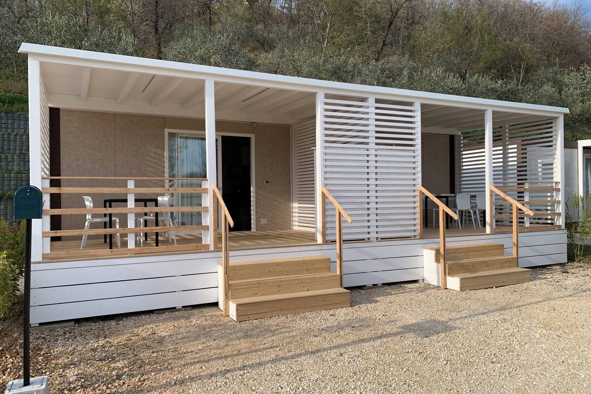 A modern, single-story mobile home with a covered porch, wooden steps, and a small outdoor seating area.