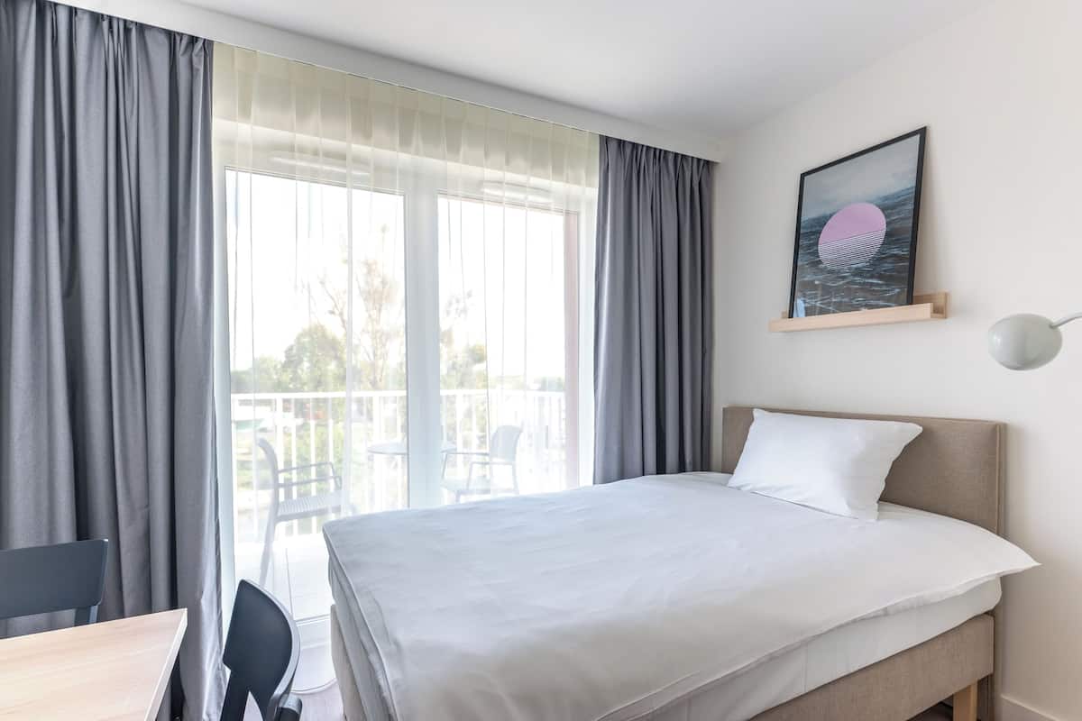 Habitación de hotel con cama, escritorio y silla. Tiene un balcón con vistas al exterior.