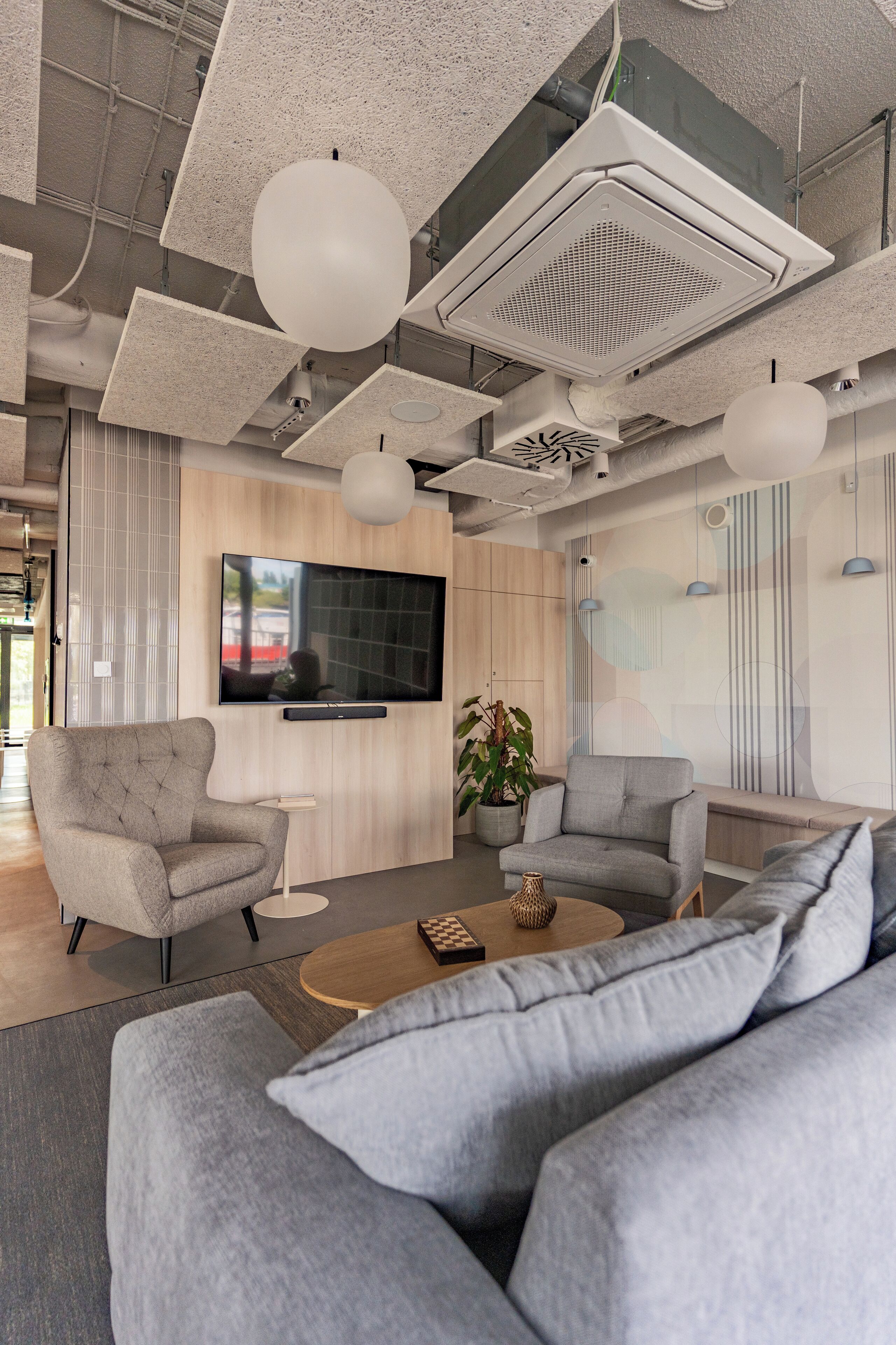 A modern living room with a large gray sofa, two armchairs, a coffee table, and a flat-screen TV mounted on the wall.