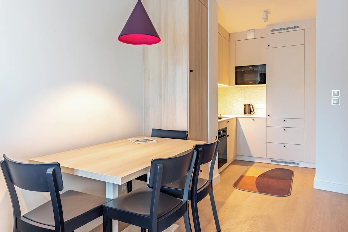 Una cocina moderna con microondas, horno y armarios. Hay una mesa de comedor con sillas y una lámpara colgante.