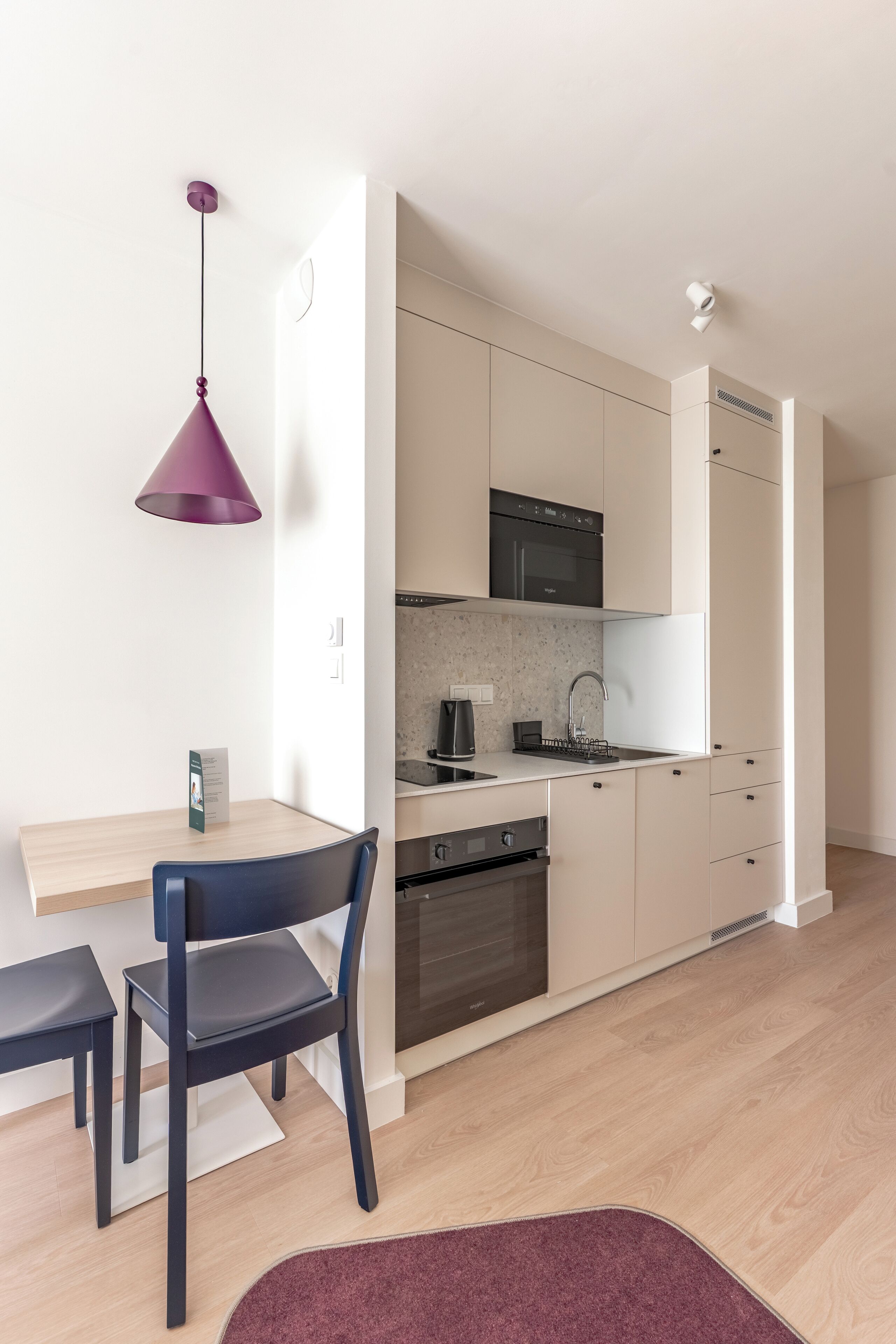 A modern kitchen with white cabinets, a black microwave, and a purple pendant light.