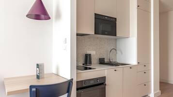 A modern kitchen with white cabinets, a black microwave, and a purple pendant light.