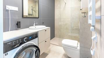 A modern bathroom with a built-in washer and dryer, a large mirror, a toilet, and a glass shower enclosure.