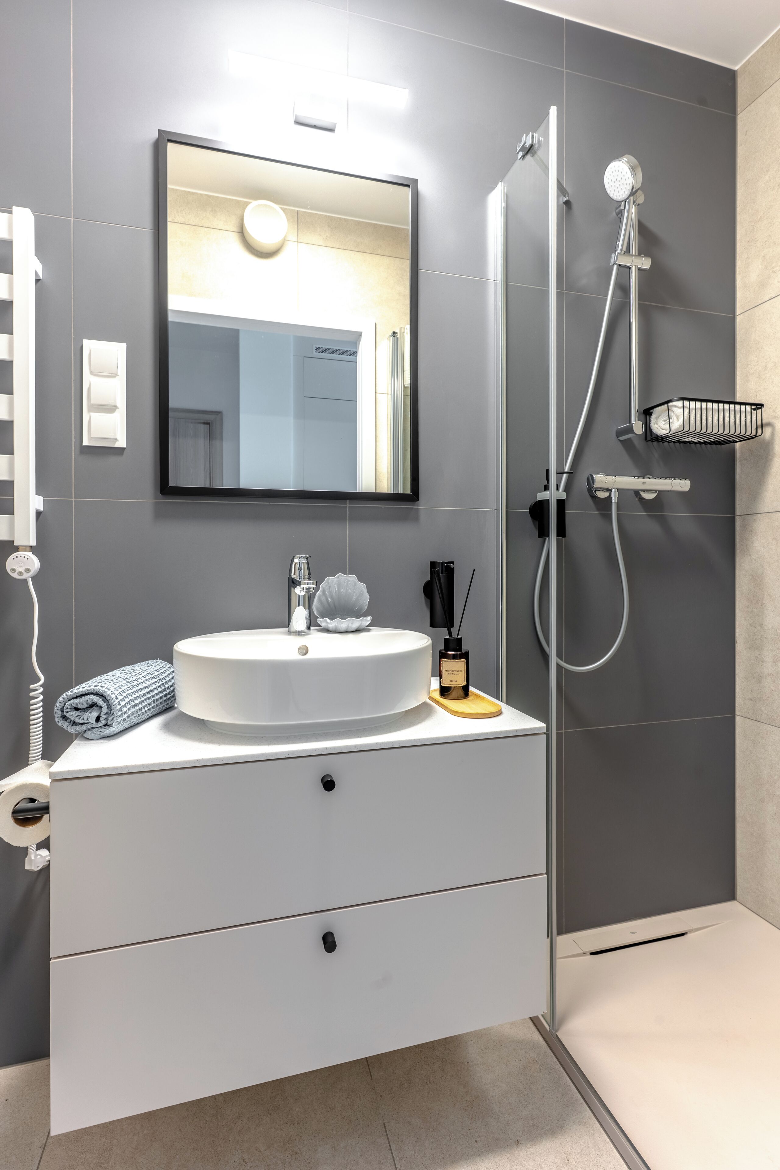 Un bagno moderno con un mobile lavabo bianco, uno specchio grande, un box doccia e un portasciugamani.
