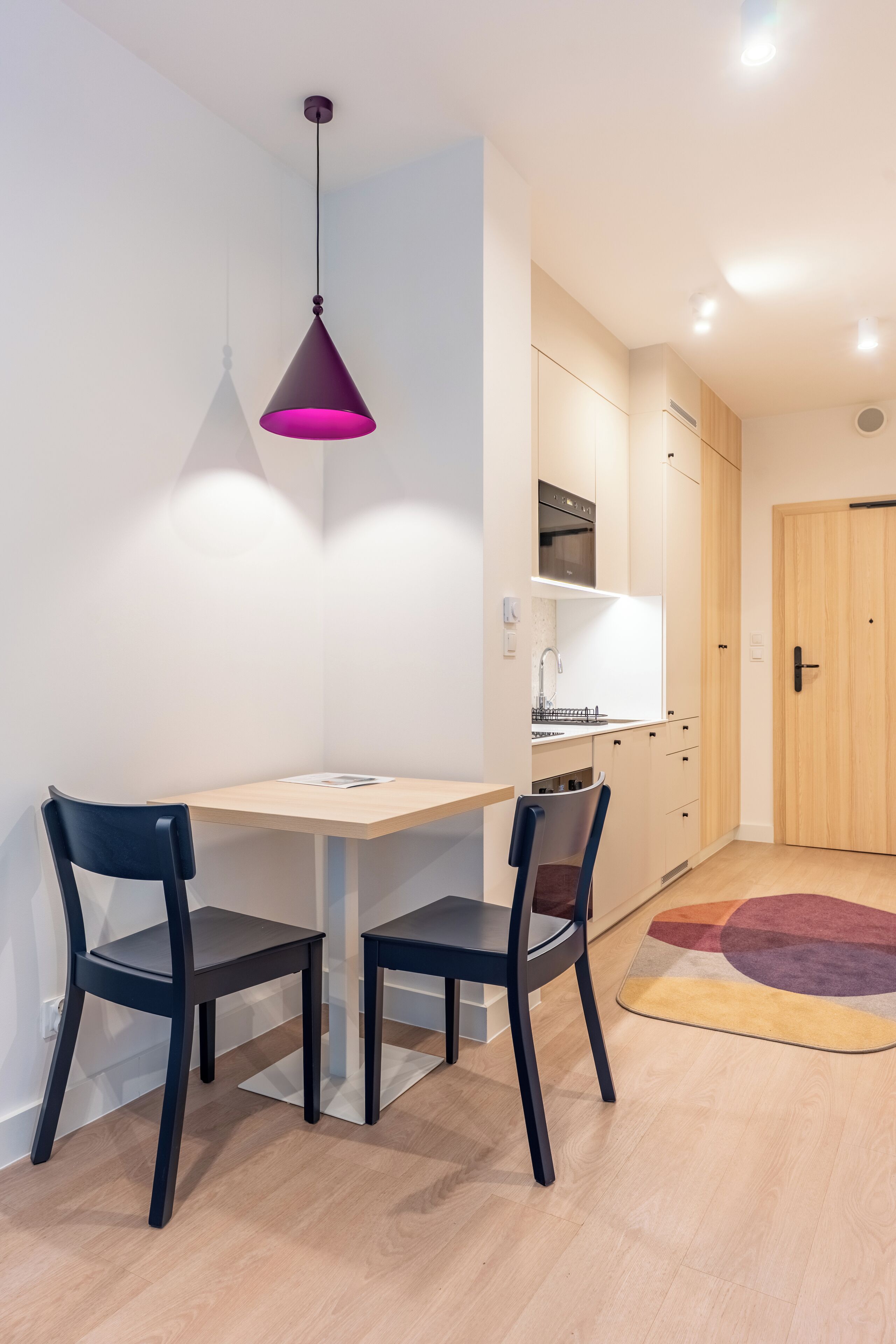 A modern kitchen with white cabinets, a wooden door, and a small dining area with two chairs and a table.