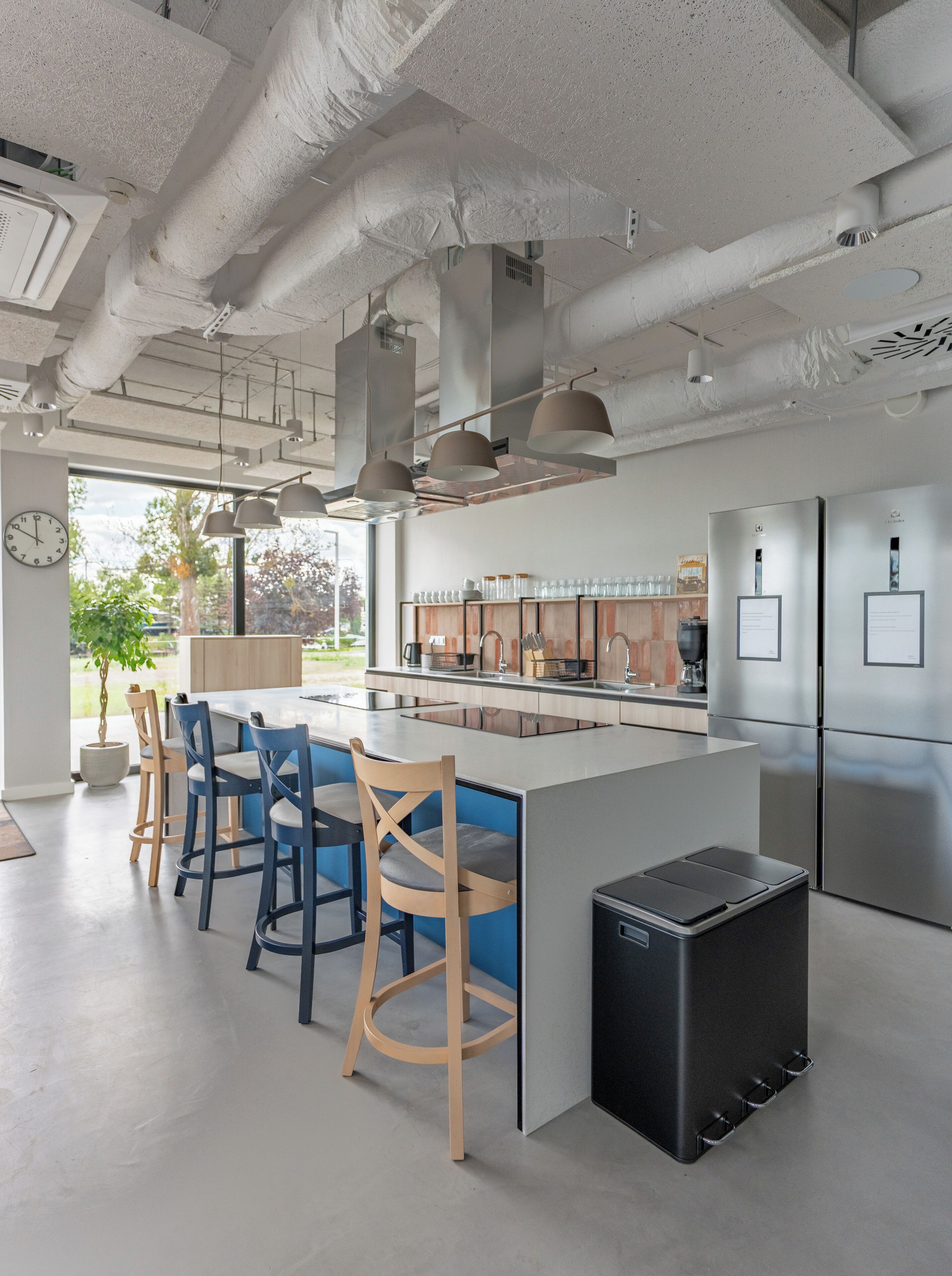 Een moderne keuken met een centraal eiland, barstoelen, roestvrijstalen apparatuur en uitzicht op de omgeving.