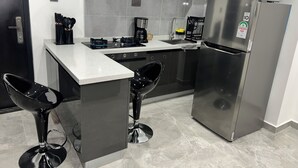 Una cocina moderna con un refrigerador de acero inoxidable, una cafetera y dos taburetes negros.