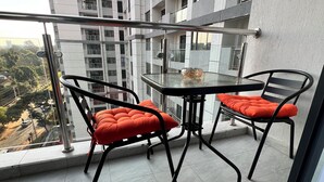 Un balcón con una mesa de vidrio y dos sillas con cojines naranja, con vista a un paisaje urbano.