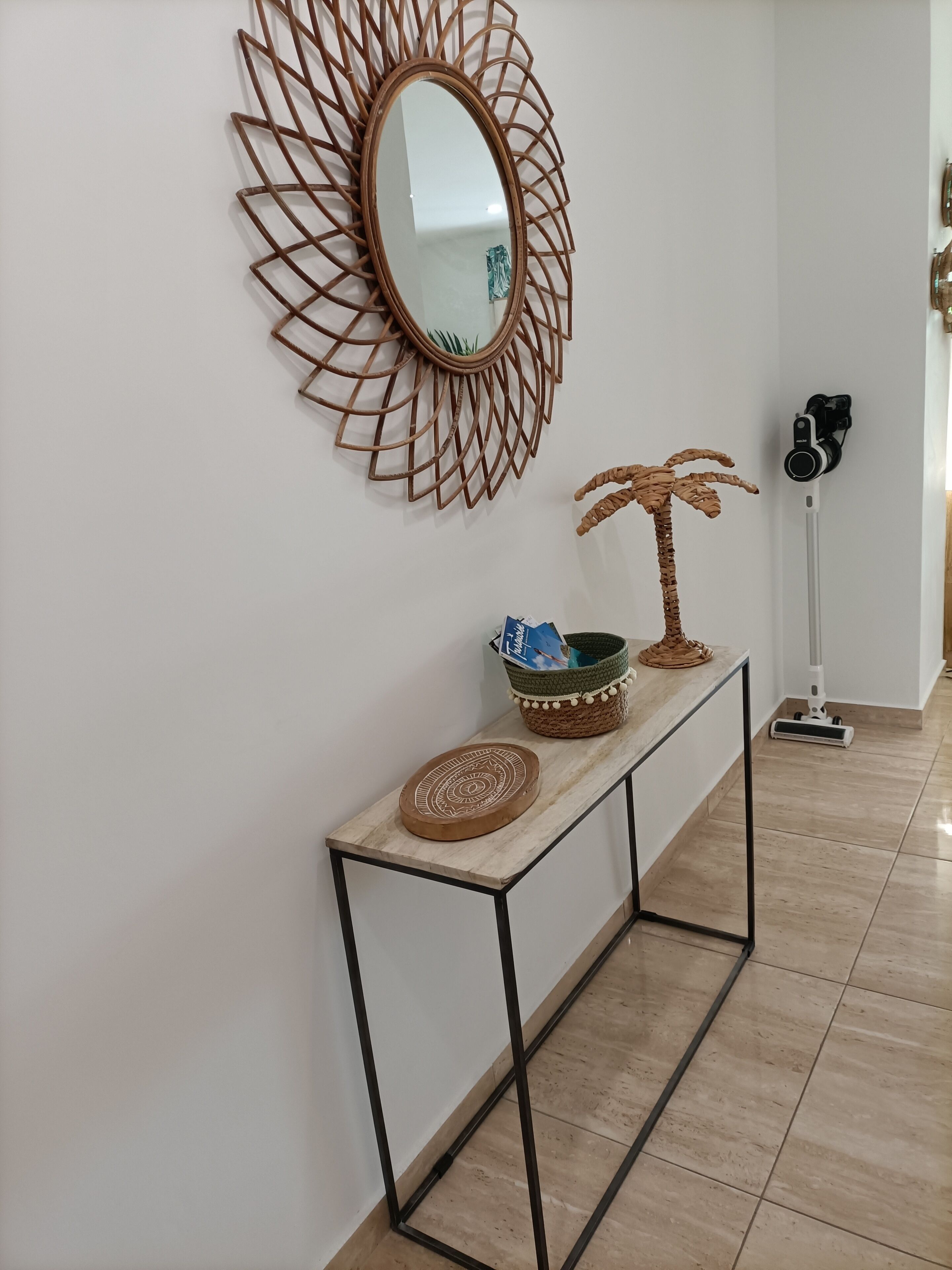 A hallway with a decorative mirror, a woven palm tree, a woven basket, and a woven tray on a console table.