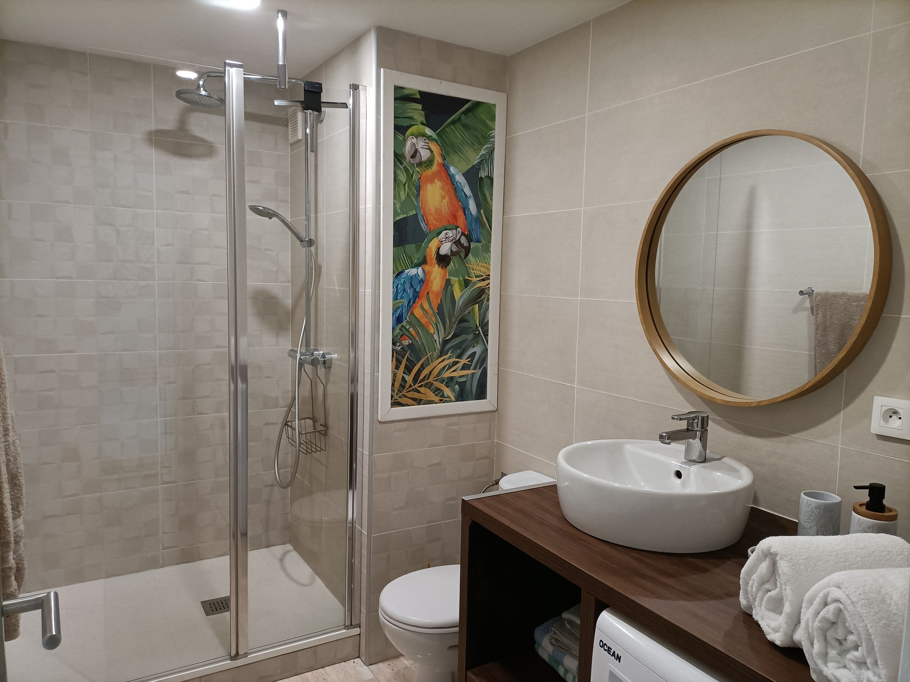 A modern bathroom with a glass-enclosed shower, a white sink, a toilet, and a wooden vanity.