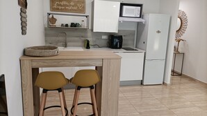 Une cuisine compacte équipée d’un four à micro-ondes, d’une machine à café et d’un réfrigérateur. On y trouve deux tabourets au comptoir et un élément décoratif mural au-dessus de l’évier.