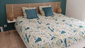 Une chambre moderne avec un mur de couleur turquoise, une tête de lit en bois à lattes, une couvre-lit à motifs et un élément décoratif mural.