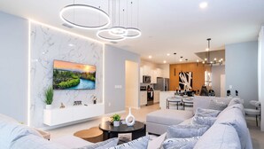 Un salon moderne avec un mur en marbre, un téléviseur à écran plat, un canapé, une table basse et une cuisine en arrière-plan.