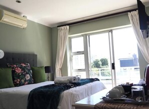 Ein Hotelzimmer mit Bett, Tisch, einem fenster mit Vorhängen und einer Klimaanlage.