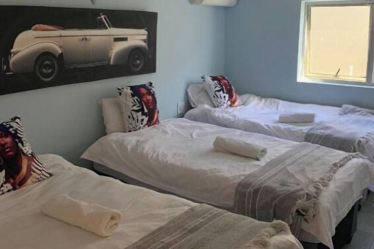 A hotel room with three single beds, a wall-mounted air conditioner, and a window with a view.